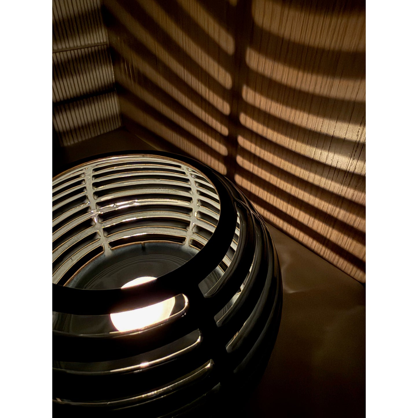 Decorative ceramic candle holder with grid pattern casting shadows on a wall