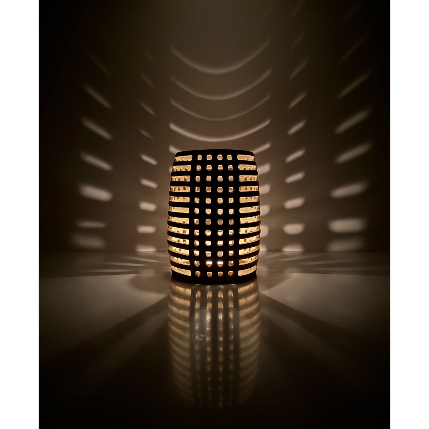 Decorative ceramic candle holder with grid pattern casting shadows on a wall