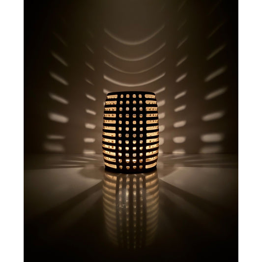 Decorative ceramic candle holder with grid pattern casting shadows on a wall