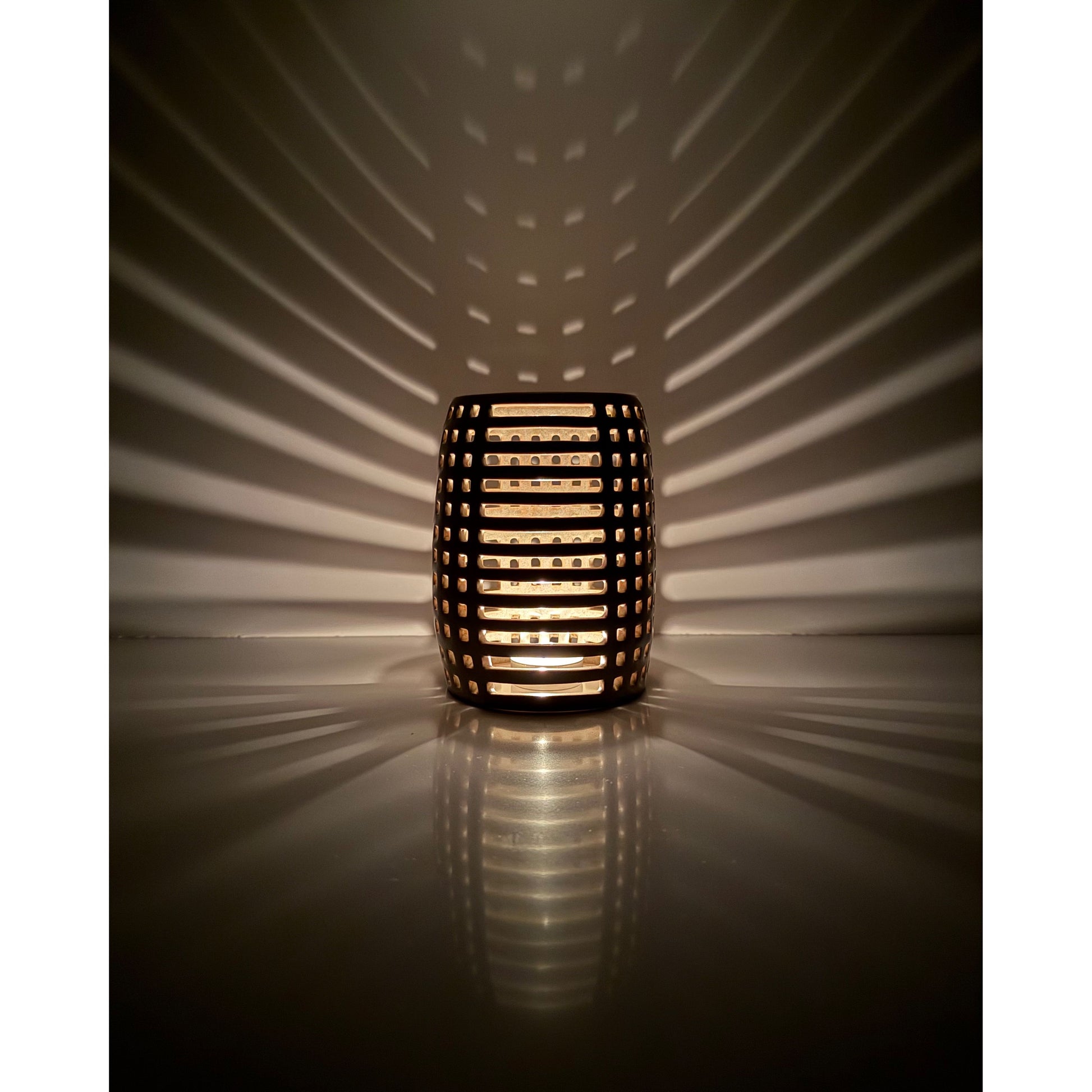 Decorative ceramic candle holder with grid pattern casting shadows on a wall