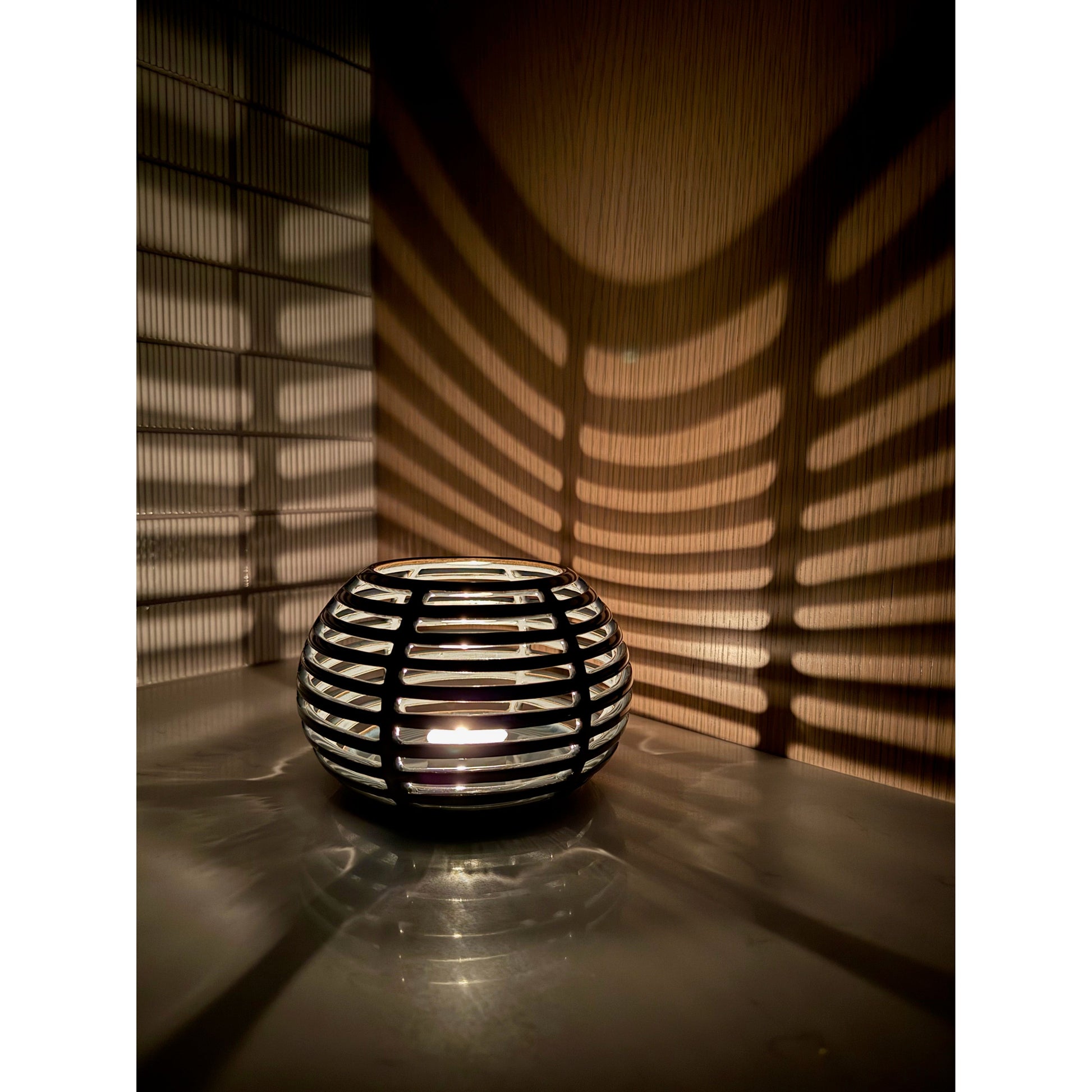 Decorative ceramic candle holder with grid pattern casting shadows on a wall