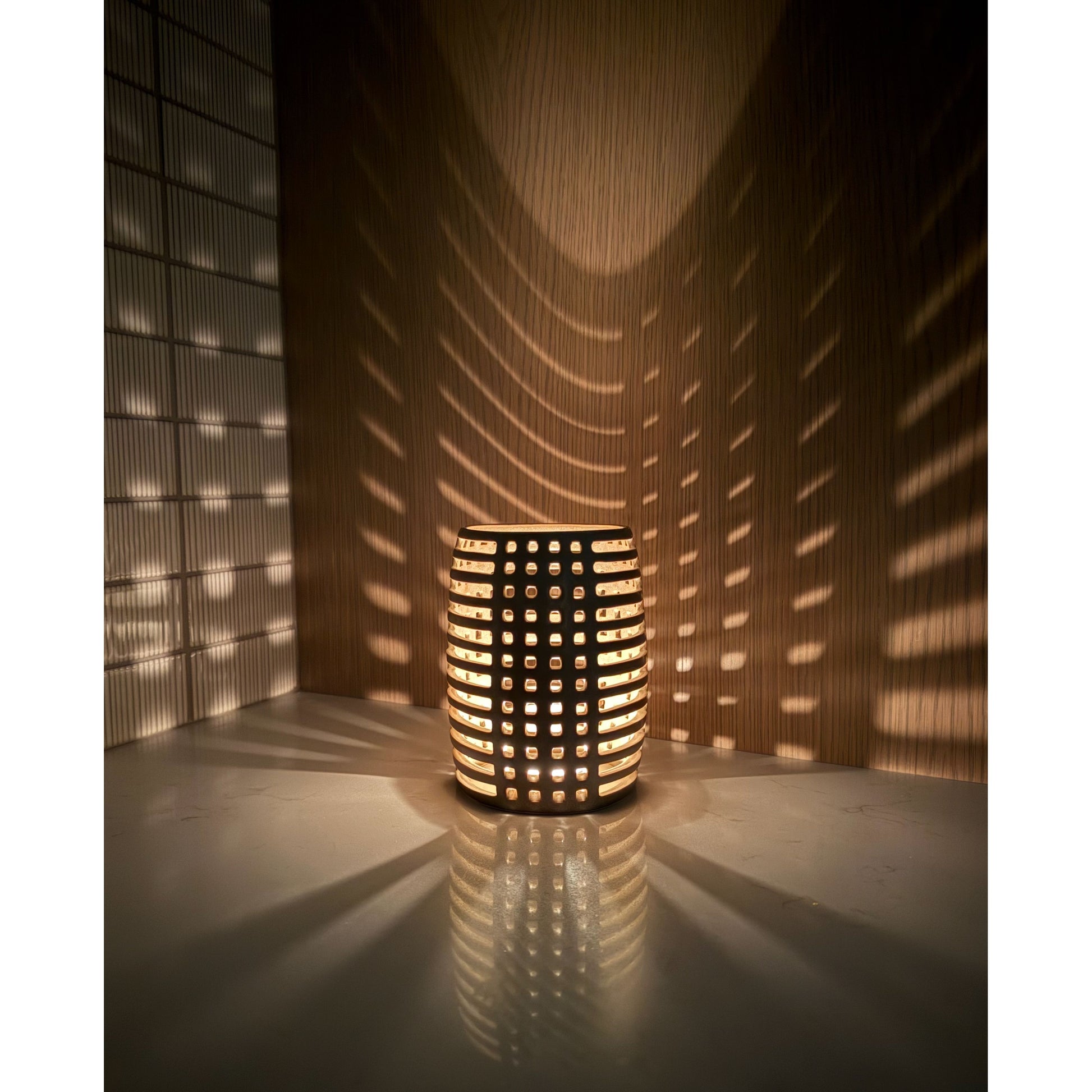 Decorative ceramic candle holder with grid pattern casting shadows on a wall