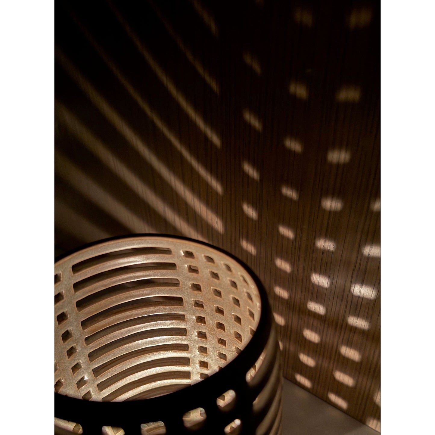 Decorative ceramic candle holder with grid pattern casting shadows on a wall